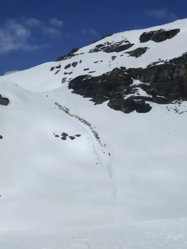 Snow-covered mountain landscape during Rupin Pass Trek with dark rocks and blue sky.
