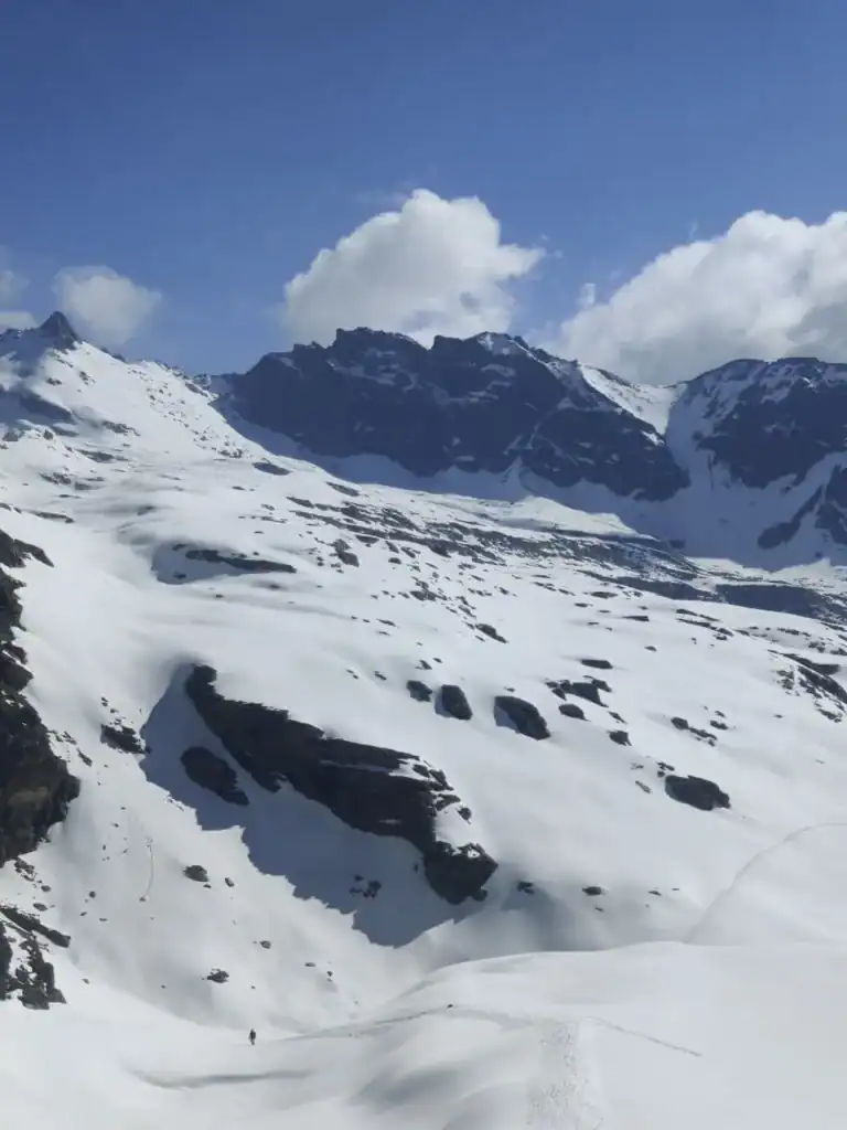Snow-covered mountain landscape during Rupin Pass Trek with blue sky and clouds.