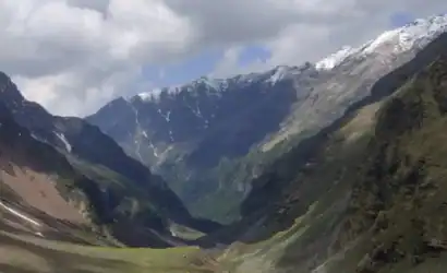 Scenic view of mountain valley with snow-capped peaks and cloudy sky.